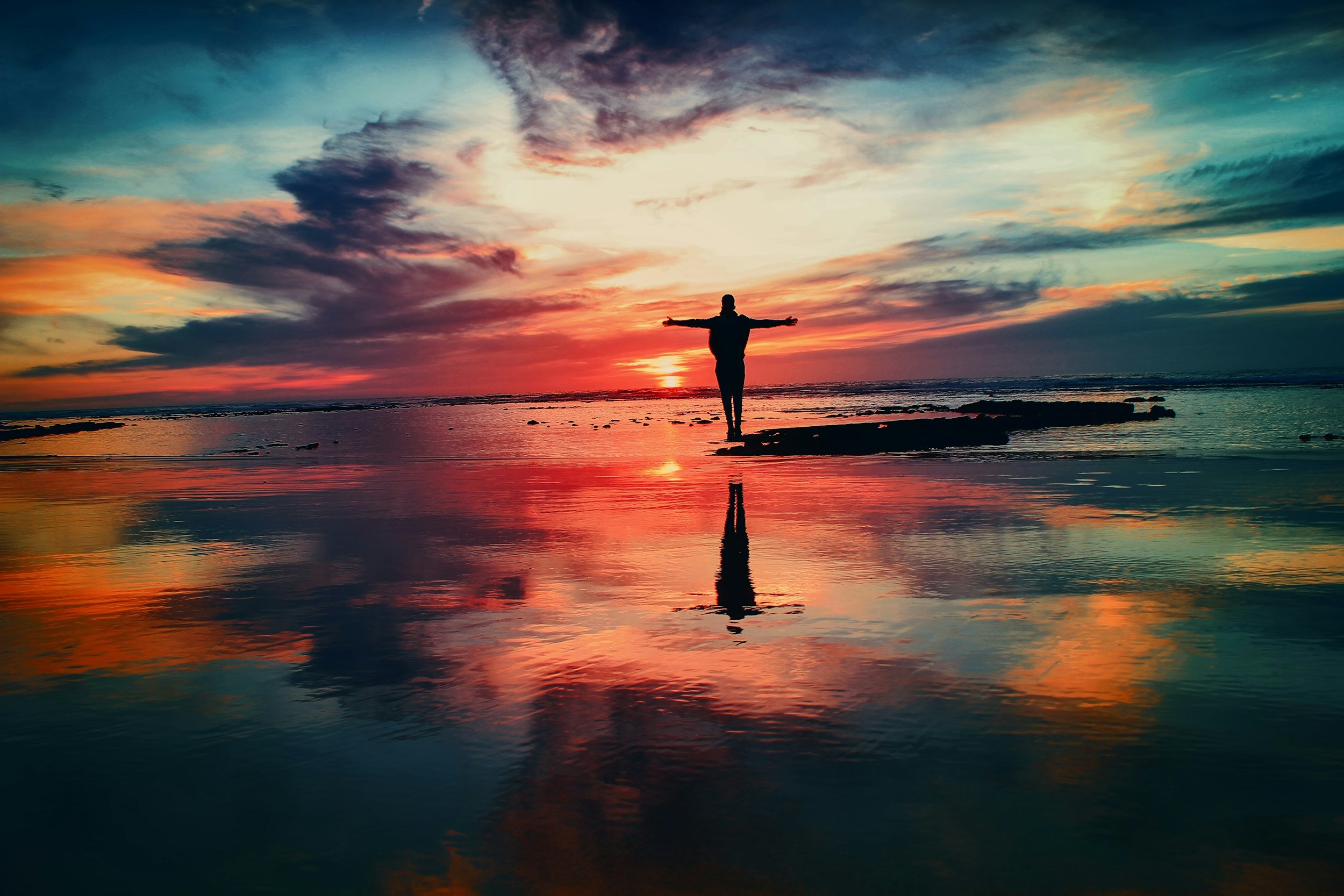 silhouette of man standing on beach at sunset with colourful sky