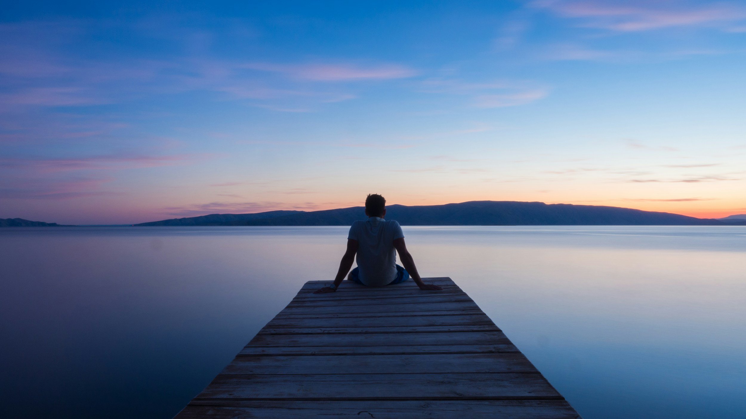 man sitting at edge of pier